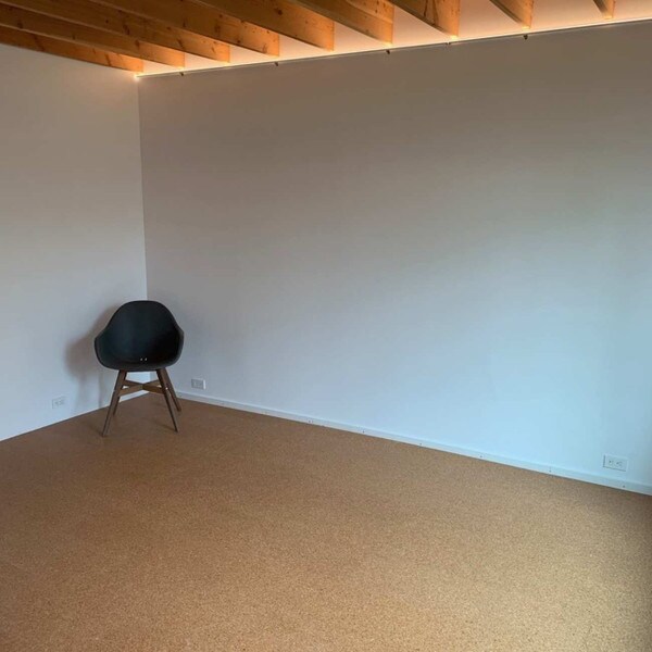 Pebble cork flooring in a large open room with a single chair, white walls and wooden ceiling beams.